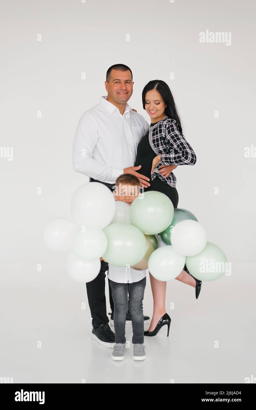 Una familia joven y feliz con un hijo está esperando a un nuevo miembro de la familia. Una mujer embarazada con un niño y su marido están sosteniendo globos en t Foto de stock