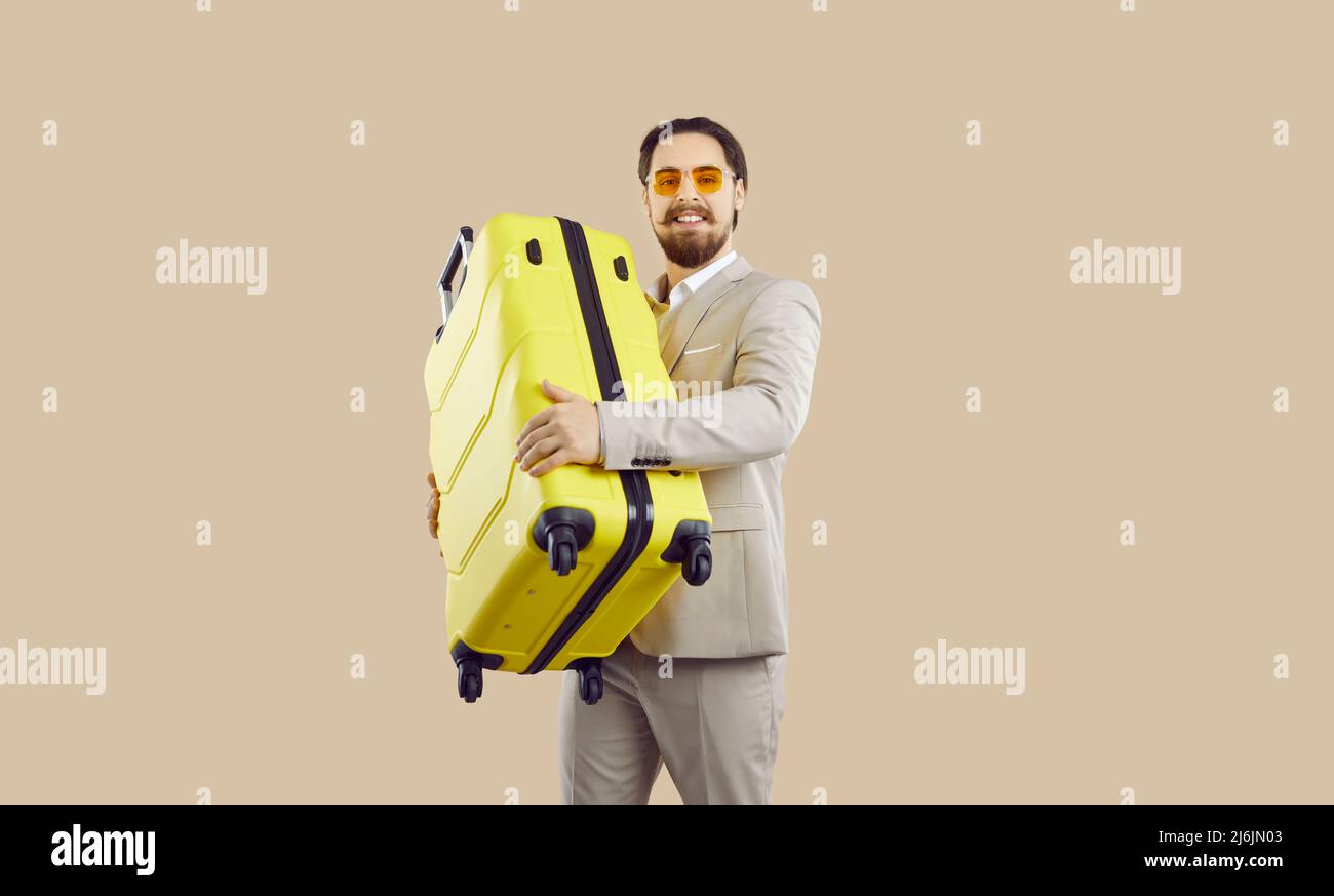 Un hombre de negocios guapo que va de vacaciones o viaje de negocios con su maleta amarilla Foto de stock