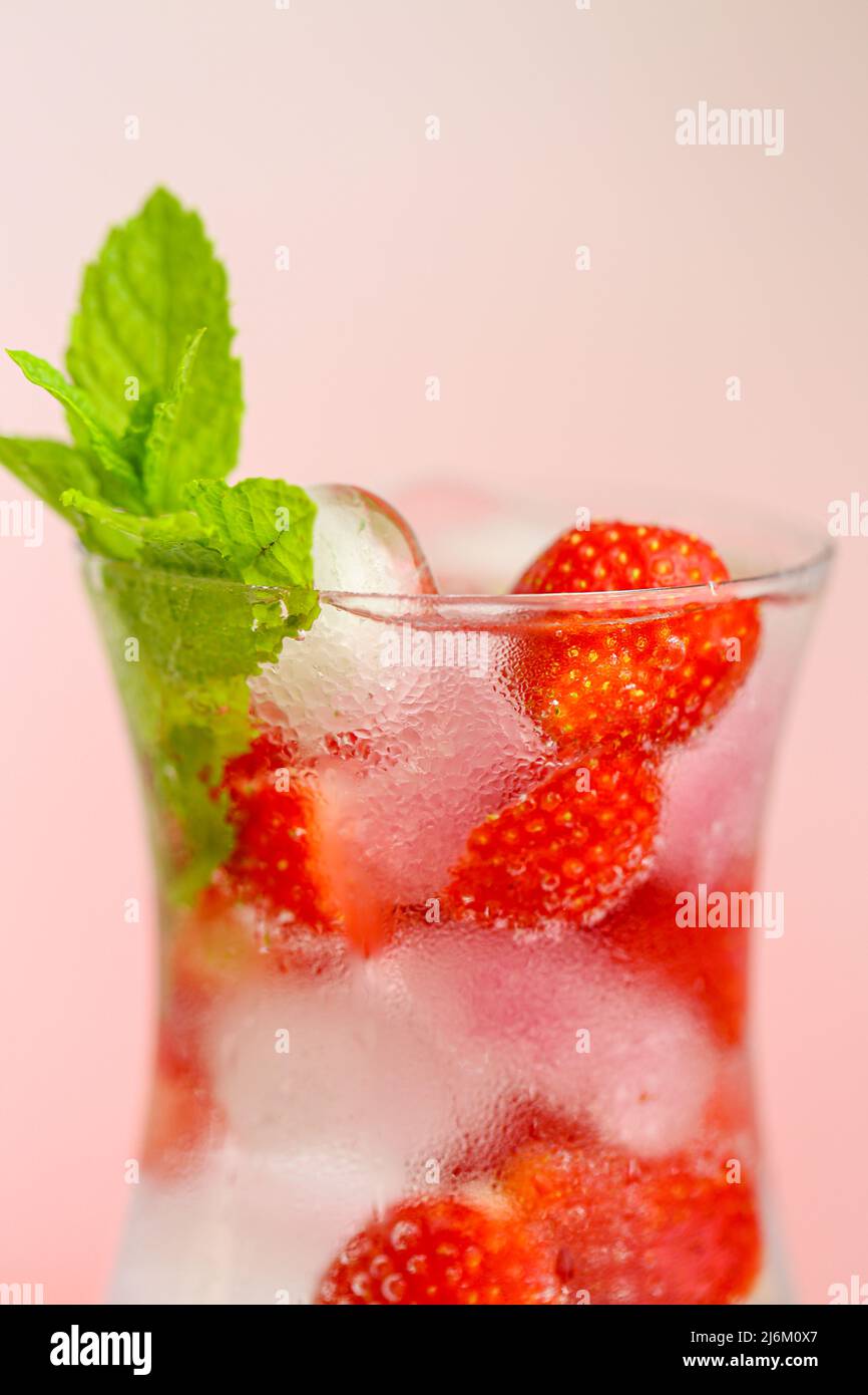 Bebidas de verano. Cóctel refrescante. Agua en vaso con hielo y fresas. Agua mineral con hielo y fresas en una copa de vidrio y madura Foto de stock