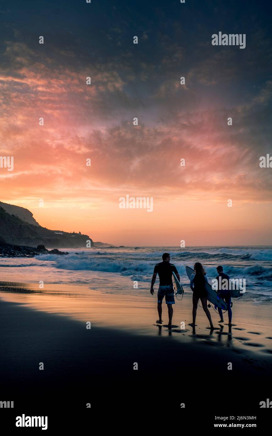 Grupo de gente de surf camina hasta las olas del océano para disfrutar de la actividad de deportes acuáticos de surf en la puesta de sol - concepto de estilo de vida activo y vacaciones de verano Foto de stock