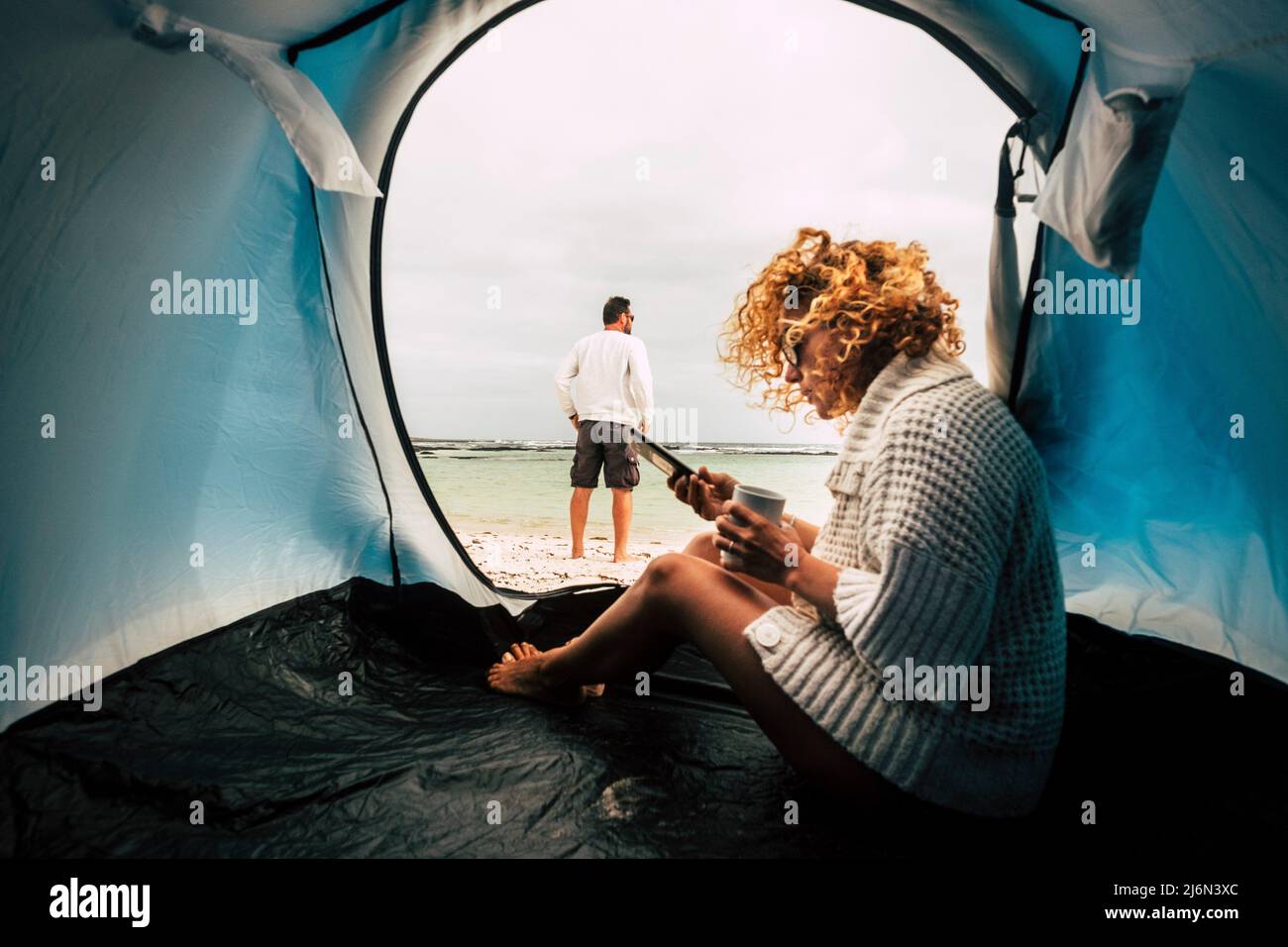 Camping tienda de vacaciones y pareja de adultos hombre y mujer disfrutando de la libertad en la playa - viajes wanderlust estilo de vida personas - mujer con phnemessaging Foto de stock