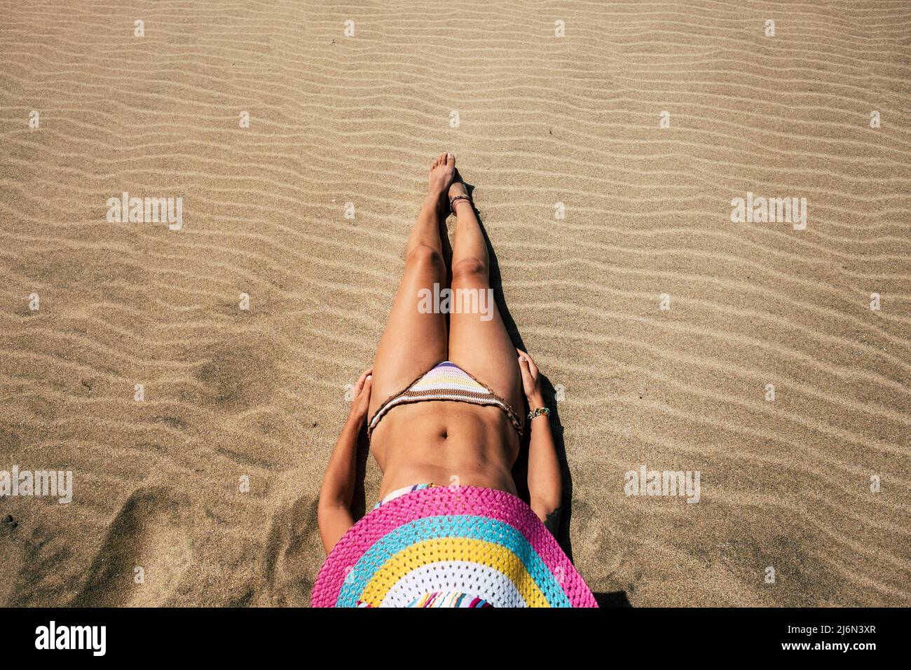 Mujer corporal agradable tumbada en la arena en la playa con colorido sombrero de paja disfrutando de vacaciones de verano solo en bikini - la gente al aire libre tiempo de relajación Foto de stock