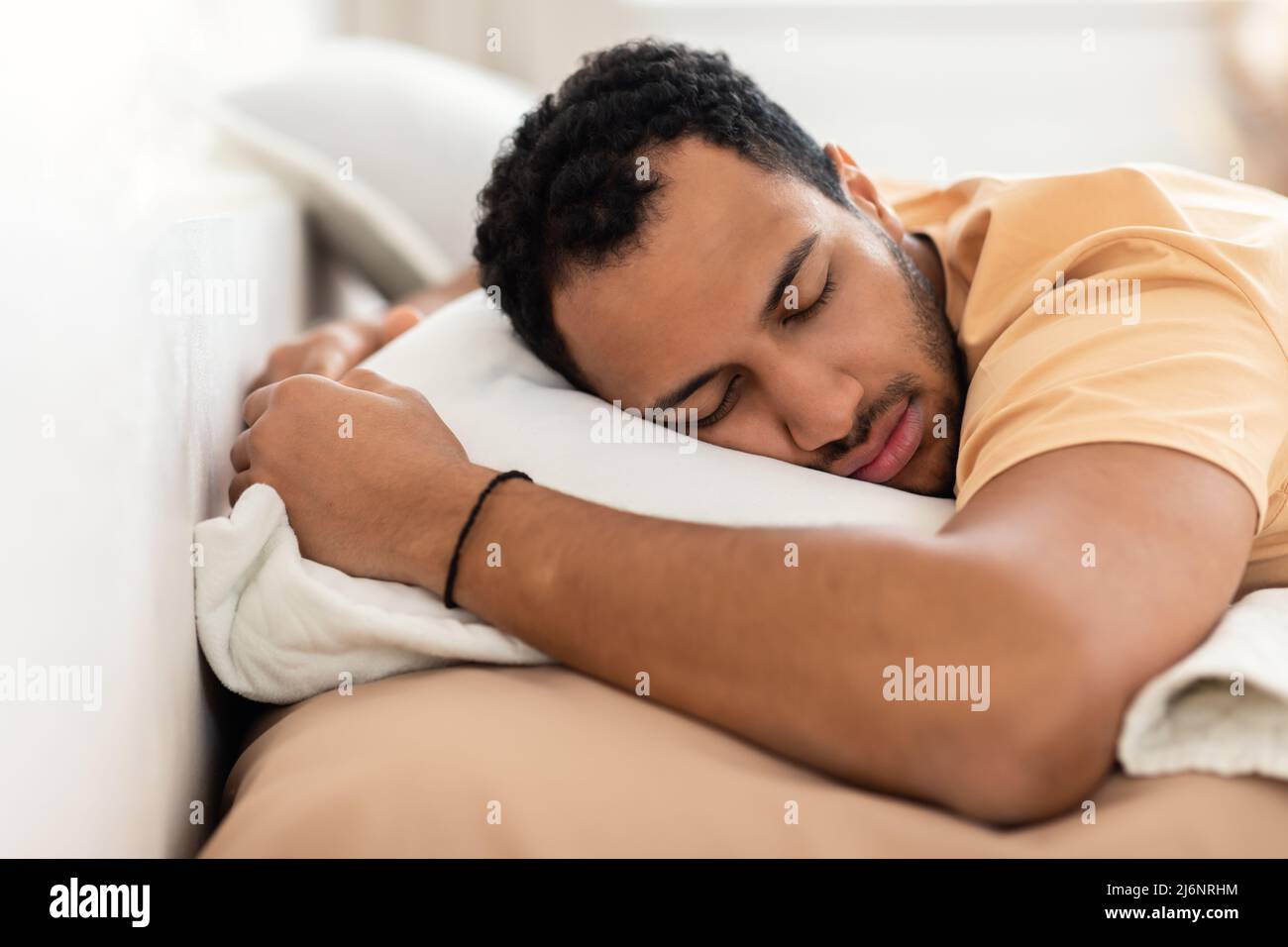 Hombre del Medio Oriente que se está durmiendo, se está tirando sobre el estómago abrazando una almohada en el interior Foto de stock