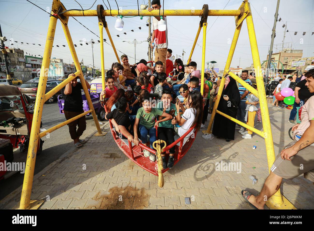03 de mayo de 2022, Irak, Bagdad: Un hombre empuja un gran columpio con varios niños en un parque de diversiones en el distrito de la ciudad de Sadr mientras celebran el segundo día de la fiesta de Eid al-Fitr, que marca el final del mes santo musulmán de Ramadán. Foto: Ameer Al-Mohammedawi/dpa Foto de stock