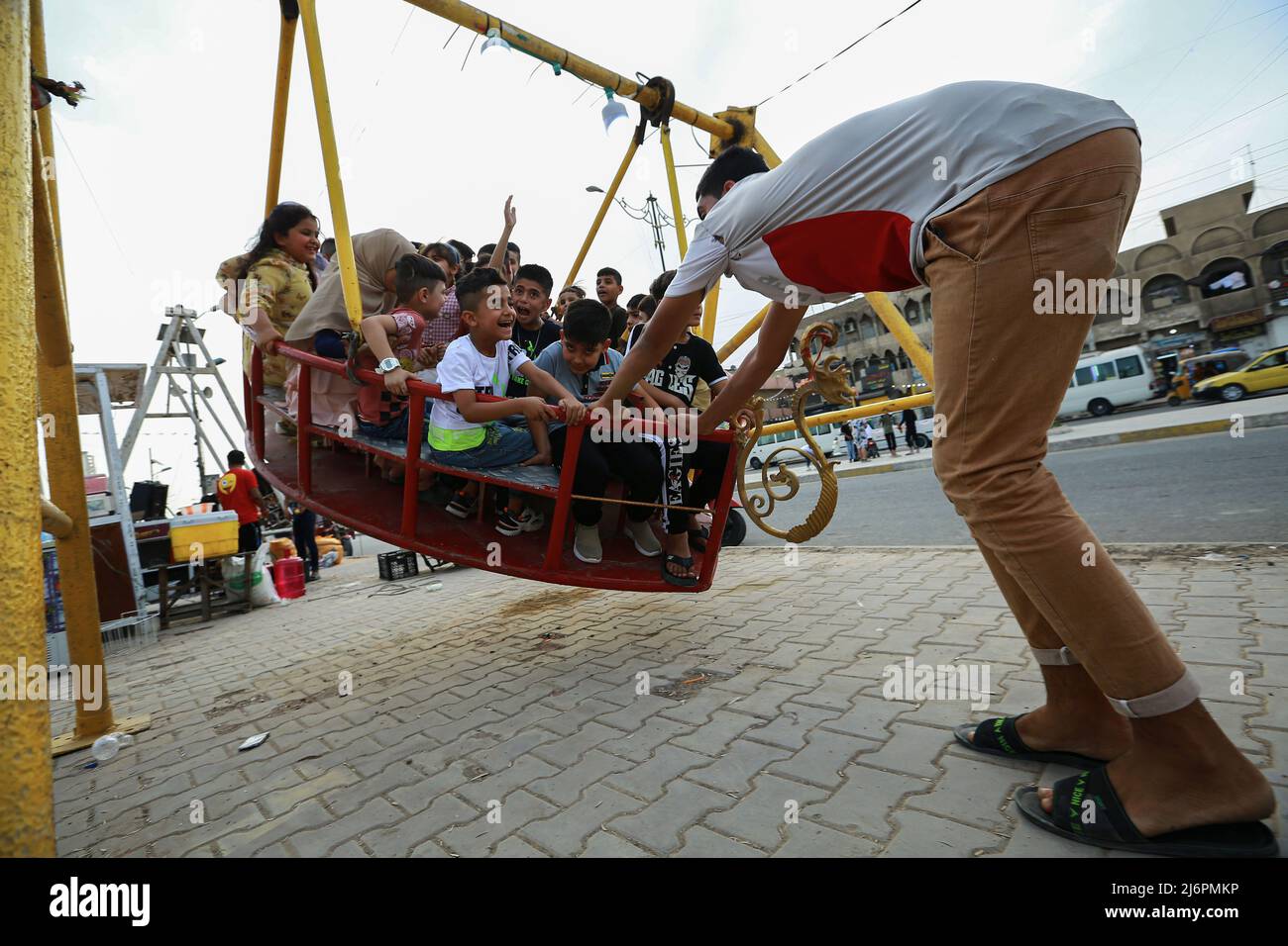 03 de mayo de 2022, Irak, Bagdad: Un hombre empuja un gran columpio con varios niños en un parque de diversiones en el distrito de la ciudad de Sadr mientras celebran el segundo día de la fiesta de Eid al-Fitr, que marca el final del mes santo musulmán de Ramadán. Foto: Ameer Al-Mohammedawi/dpa Foto de stock