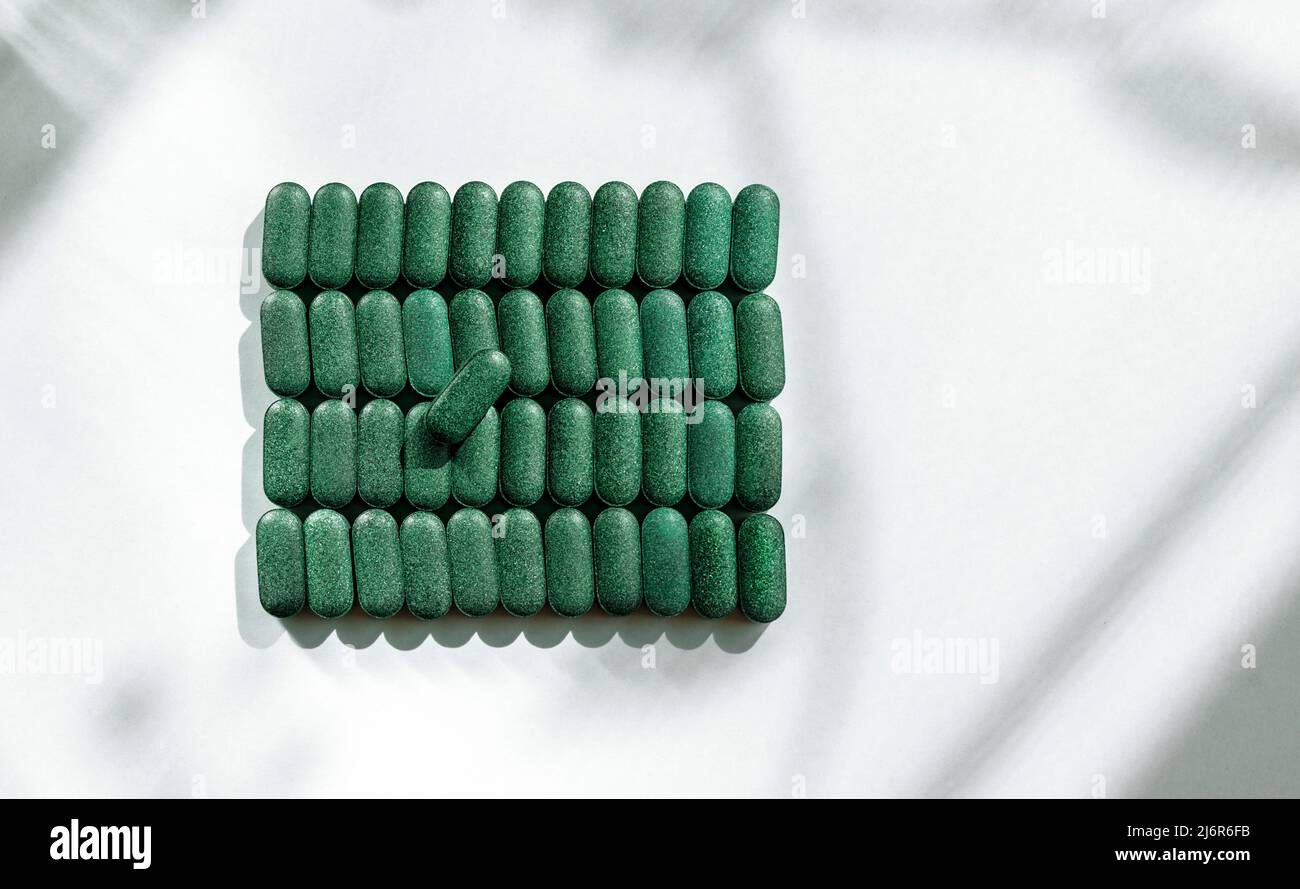 Pastillas de clorella, espirulina, cebada hierba de primer plano alineado en filas sobre fondo blanco con patrón de sombra Suplemento nutricional detox superfood h Foto de stock