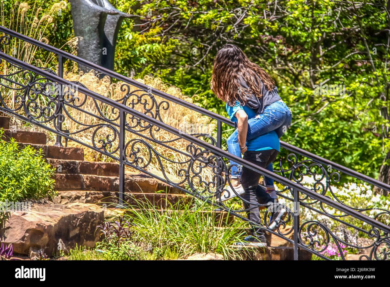 Niños de la escuela secundaria goofing alrededor en el parque - niño subiendo escaleras con niña de pelo largo que monta en piggy espalda - enfoque selectivo y movimiento desenfocado Foto de stock