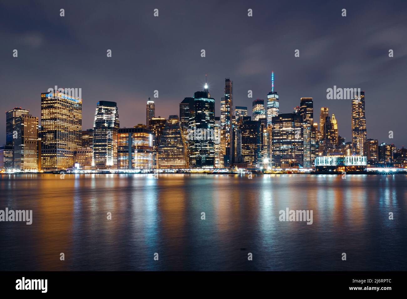 Horizonte de Manhattan por la noche con edificios iluminados en azul y amarillo para apoyar a Ucrania y el colorido río East Foto de stock