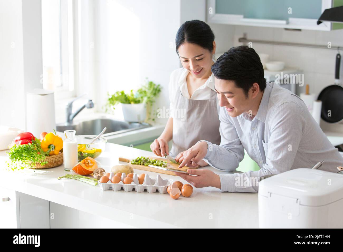 En la cocina familiar, una pareja joven disfruta cocinando juntos. Utilizan tabletas para consultar los tutoriales de cocina - foto de stock Foto de stock