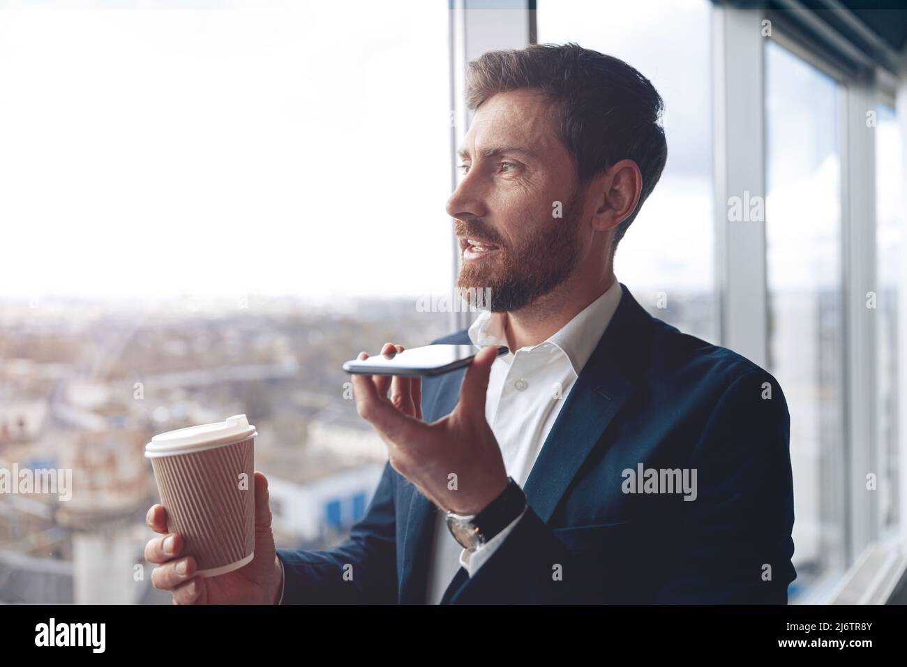 Un hombre de negocios centrado está utilizando un smartphone para grabar un mensaje de voz al socio comercial Foto de stock