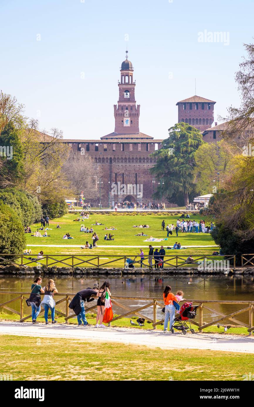 Milaneses y turistas disfrutan del Parco Sempione (parque Simplon) en Milán, Italia, con vistas a las torres del Castello Sforzesco (Castillo Sforza). Foto de stock