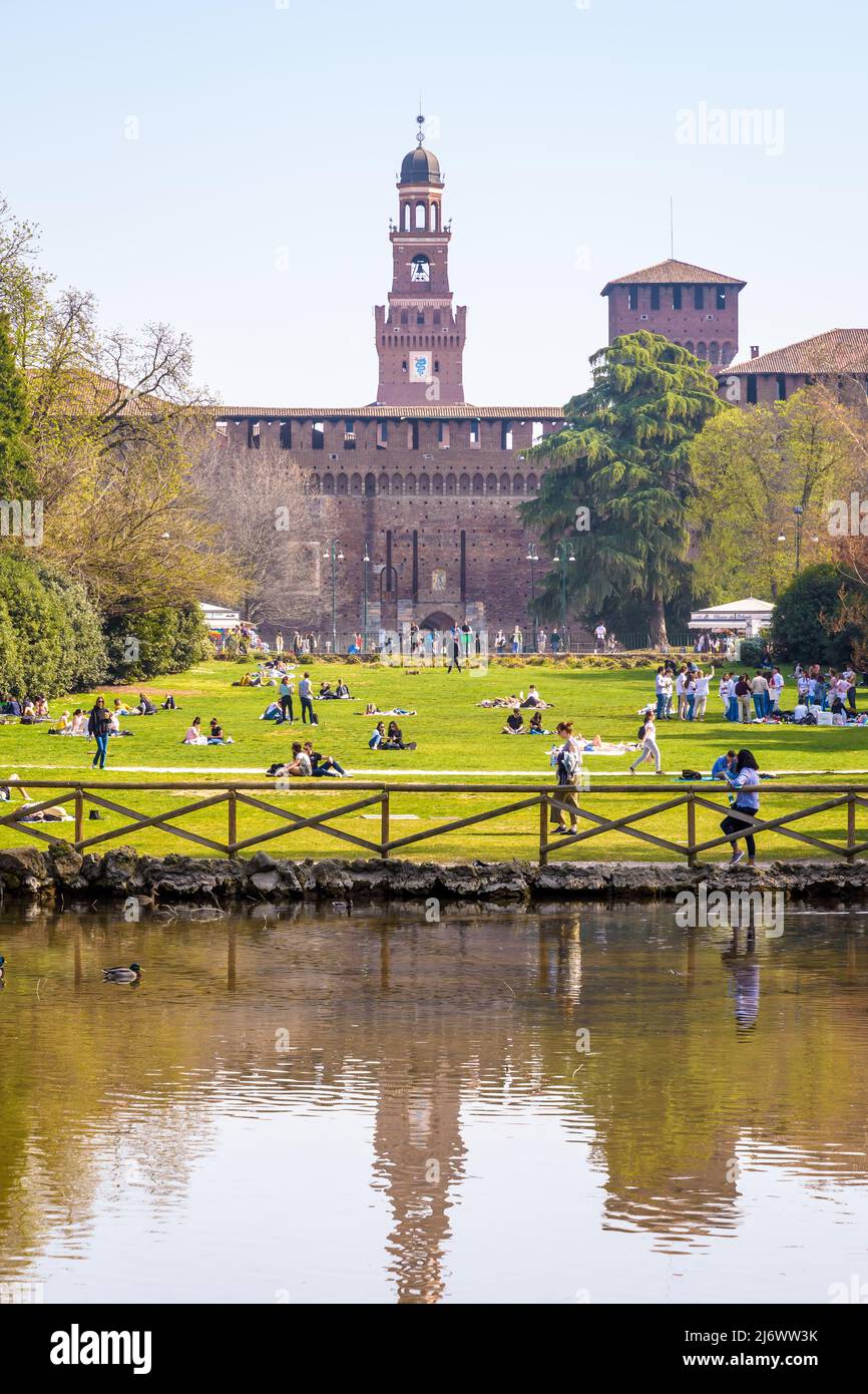 Las torres del Castello Sforzesco (Castillo de Sforza) se reflejan en el estanque del parque Simplon (Parco Sempione) en Milán, Italia, en un soleado día de primavera. Foto de stock