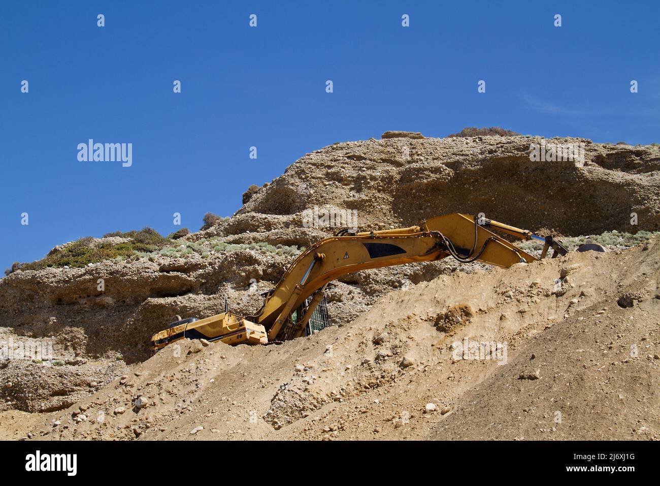 Excavadora amarilla de cadenas trabajando en la reparación de una carretera en las montañas Foto de stock