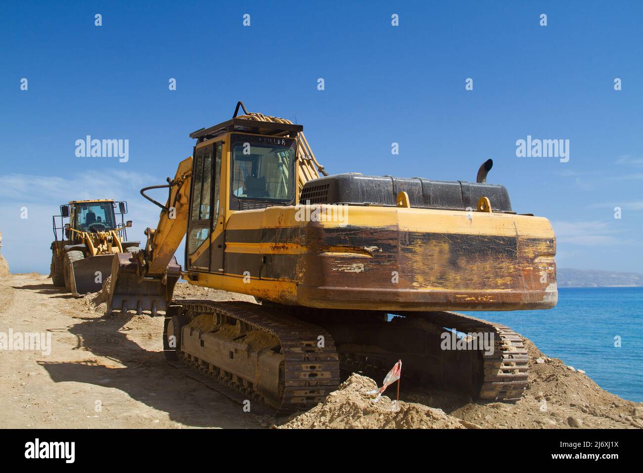 Excavadora amarilla de cadenas trabajando en la reparación de una carretera en las montañas cerca del mar Foto de stock
