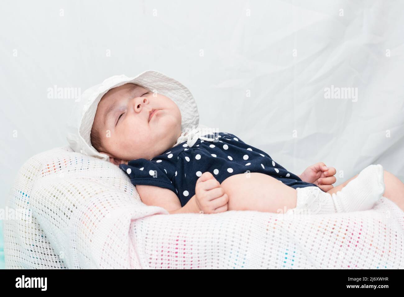 hermoso bebé caucásico durmiendo tranquilamente en una cuna pequeña, vestida con una mancha azul y un sombrero blanco. sobre un fondo blanco con espacio para copiar texto Foto de stock