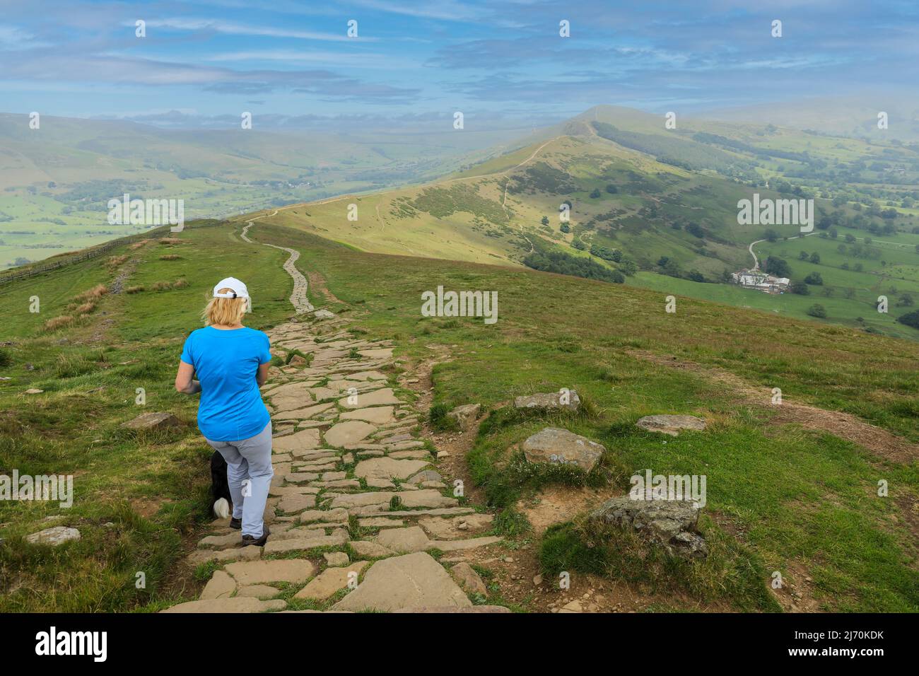 Una mujer caminando por un camino pavimentado en la cima de Mam Tor Castleton en el pico alto de Derbyshire, Parque Nacional del Distrito de los Picos, Inglaterra, Reino Unido Foto de stock