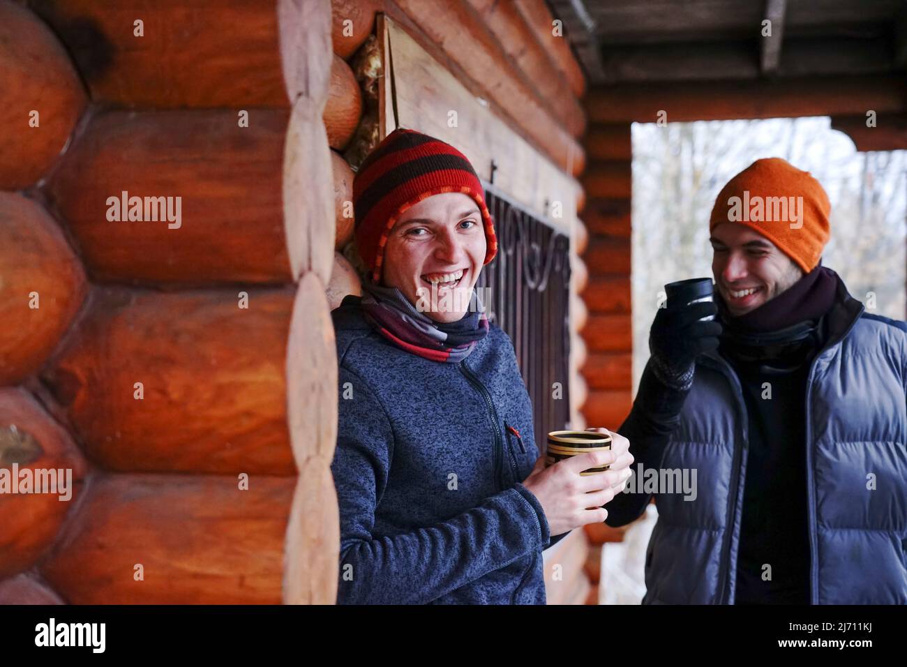 Dos chicos conversan después de esquiar. Se encuentran en el balcón de una casa de madera con ropa de invierno, beber té y relajarse. Portero de dos chicos en una estación de esquí Foto de stock