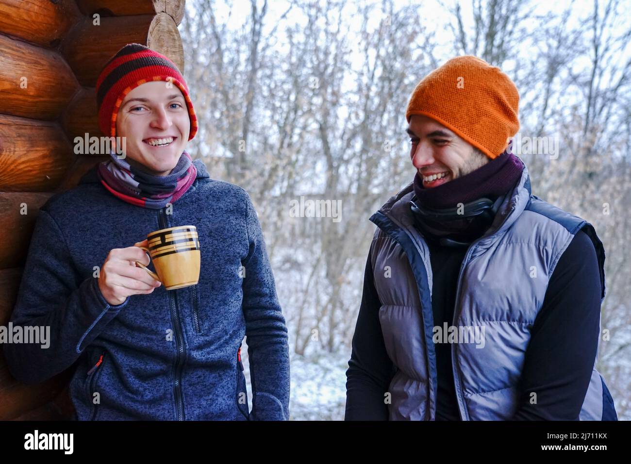 Dos chicos conversan después de esquiar. Se encuentran en el balcón de una casa de madera con ropa de invierno, beber té y relajarse. Portero de dos chicos en una estación de esquí Foto de stock
