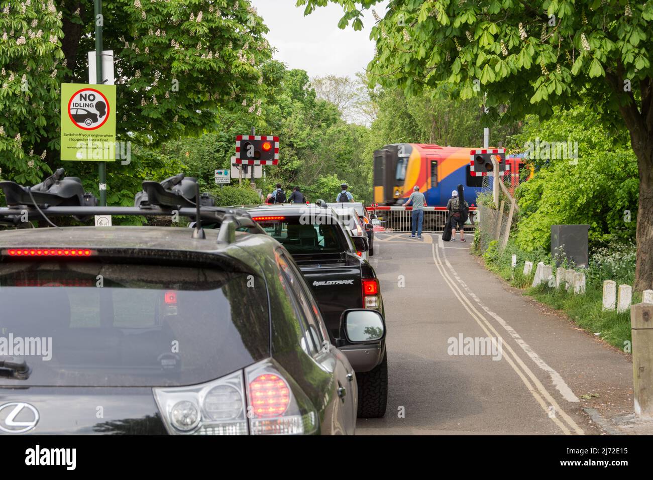 Los coches estacionarios hacen cola y se ponen en ralentí mientras un tren South Western Railway pasa la caja de señal Vine Road de Network Rail en Barnes, Londres, SW13, Inglaterra, Reino Unido Foto de stock