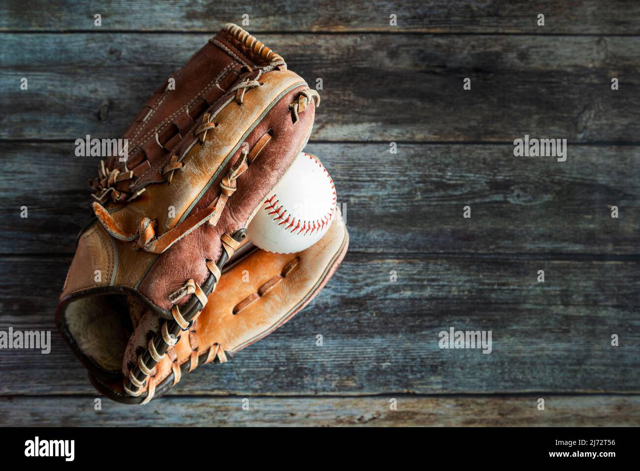 Guante de cuero de béisbol o sóftbol con pelota sobre fondo rústico de madera con espacio de copia. Foto de stock