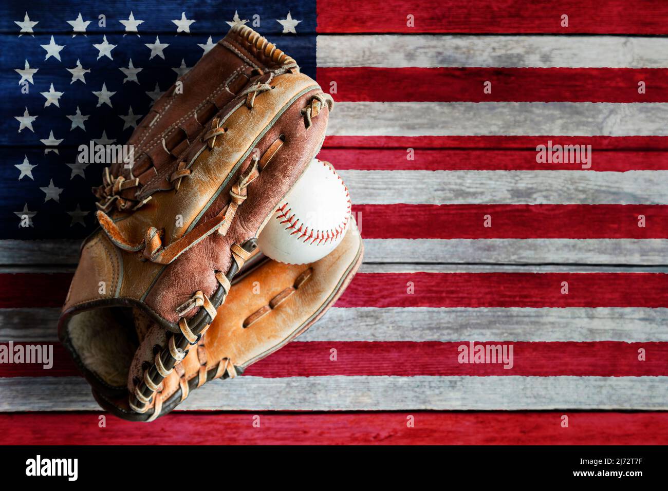 Guante de cuero de béisbol o sóftbol con pelota sobre fondo rústico de madera con bandera estadounidense pintada y espacio de copia. Foto de stock