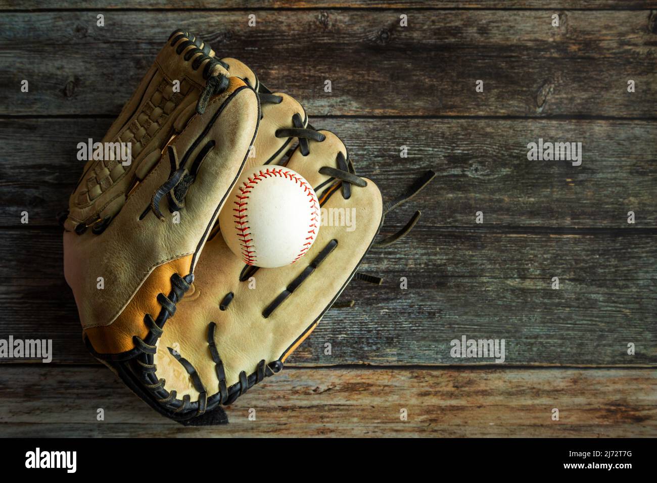 Guante de cuero de béisbol o sóftbol con pelota sobre fondo rústico de madera con espacio de copia. Foto de stock