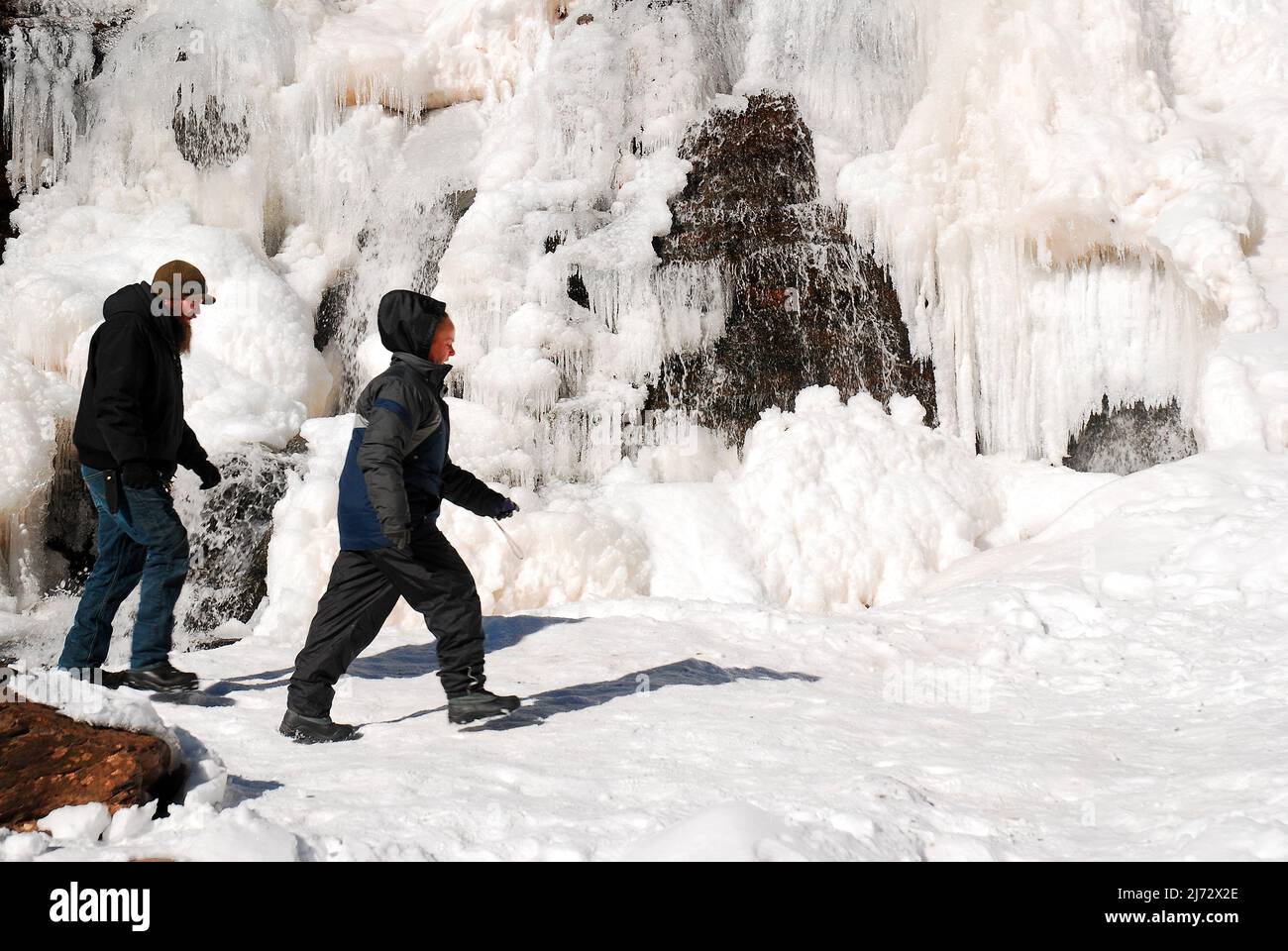 Una joven pareja de adultos camina por una cascada congelada Foto de stock