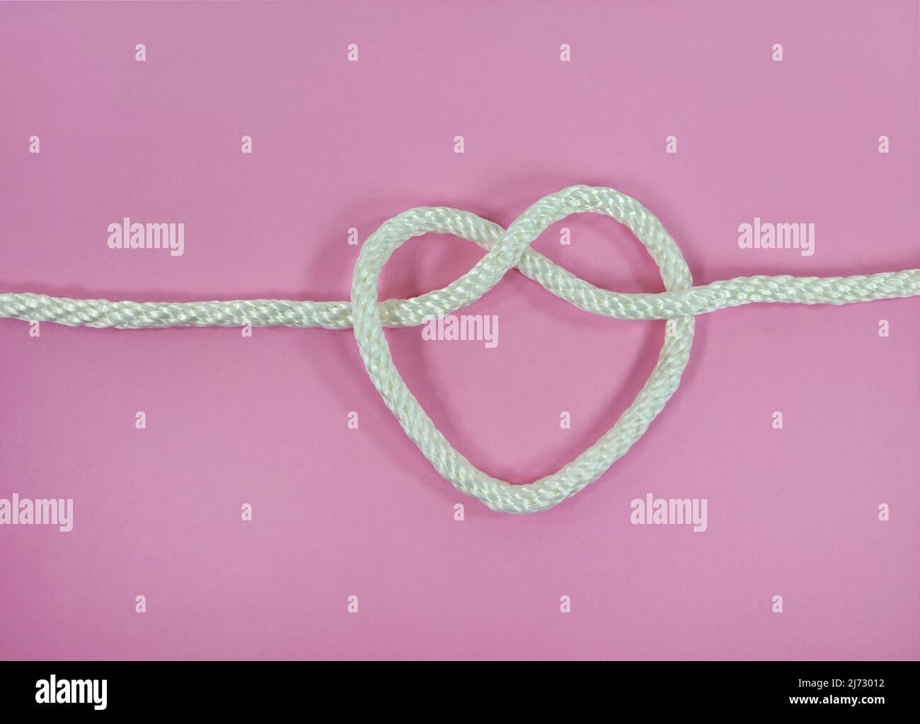 Primer plano de la cuerda blanca en forma de corazón se sabe sobre fondo rosa Foto de stock