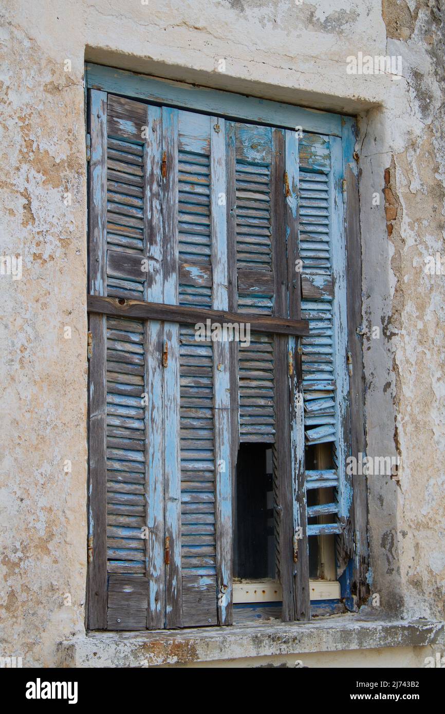 Persianas de color azul pálido envejecidas en la ventana de un edificio en ruinas Foto de stock