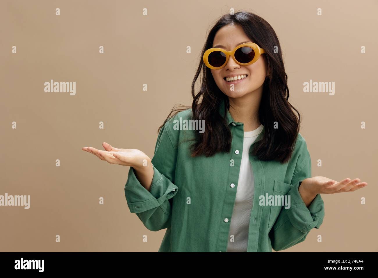 Disfrutando de la joven coreana en camisa verde caqui con estilo gafas  levantar las palmas de las manos sostener objetos invisibles posando  aislados sobre un estudio color beige pastel Fotografía de stock -