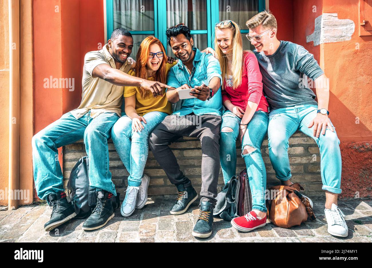 Jóvenes multiétnicos que usan el smartphone en el patio trasero del edificio de la escuela - Felices amigos en el estado de ánimo adicto con teléfonos inteligentes móviles - Concepto de tecnología Wit Foto de stock