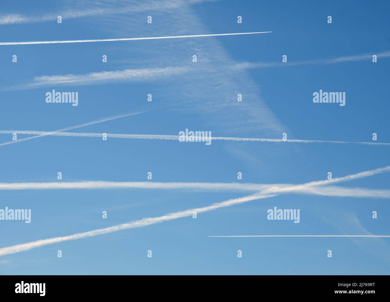 Varios aviones se contrainan cruzando el cielo azul en un estado de sobrevuelo, con dos aviones haciendo activamente nuevos senderos en la parte superior e inferior, a la dirección opuesta Foto de stock