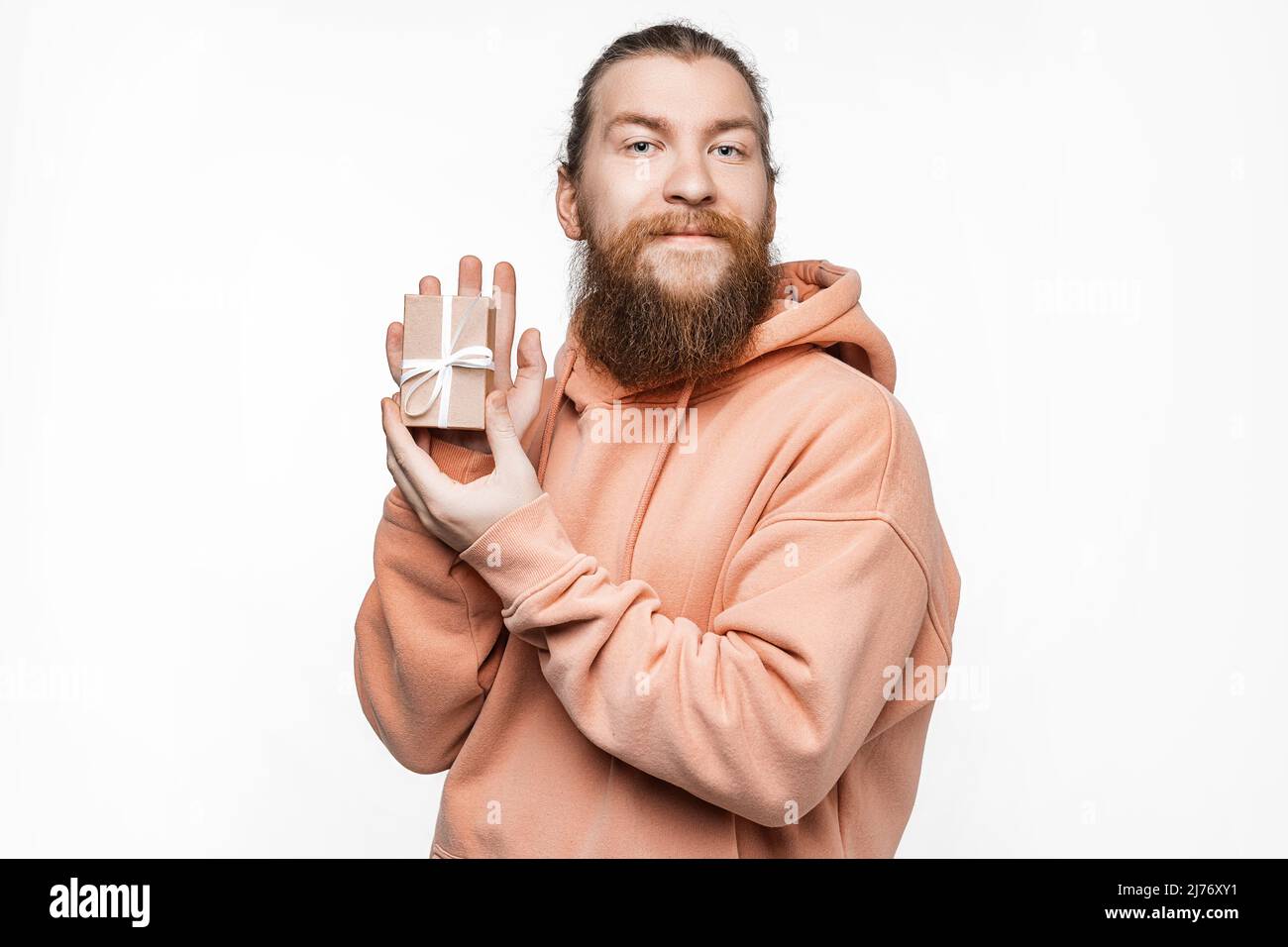 Hombre escandinavo guapo sosteniendo regalo y puntos para presentar aislados sobre fondo gris. Hombre con peinado de jengibre y barba en una sudadera. Concepto Foto de stock