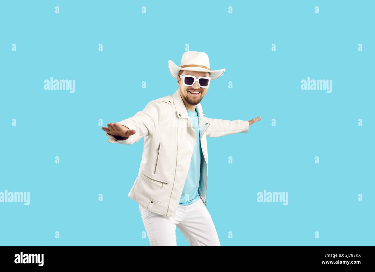 Feliz joven en chaqueta de cuero blanco, sombrero de vaquero y gafas de sol bailando en el estudio Foto de stock