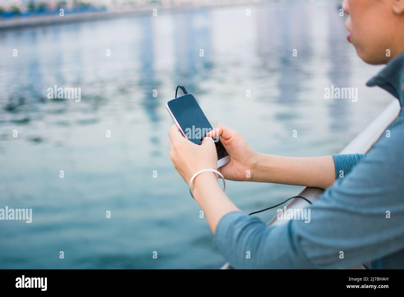Mujer con traje deportivo con teléfono inteligente con cable de auriculares conectado sobre el agua con espacio de copia Foto de stock
