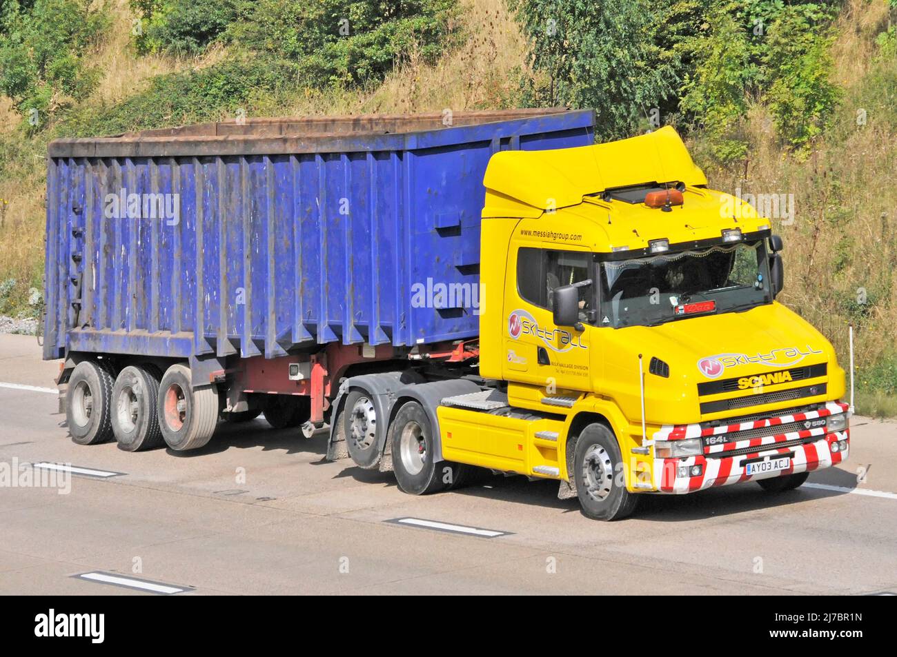 Transportista contratista de negocios amarillo deshuesado hgv SCANIA camión azul sin marcar sucio artillado volquete remolque que conduce por la autopista inglesa del Reino Unido Foto de stock