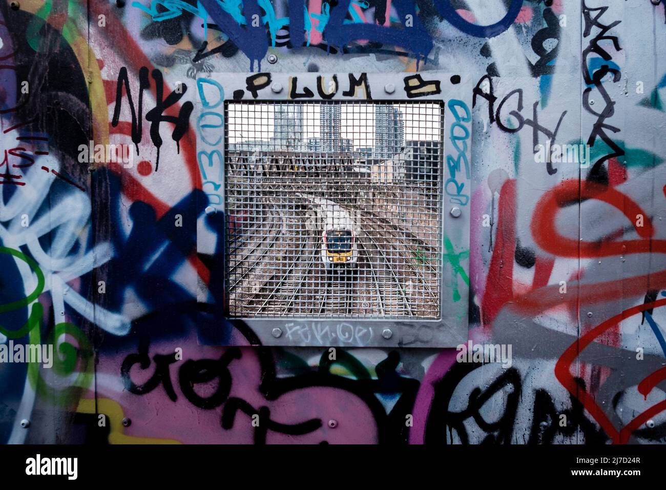 Tren que pasa por debajo de la pasarela cubierta de graffiti, al este de Londres, Reino Unido Foto de stock