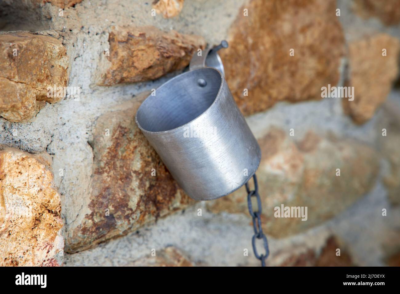 Taza de aluminio colgada en una cadena sobre una pared de piedra Foto de stock
