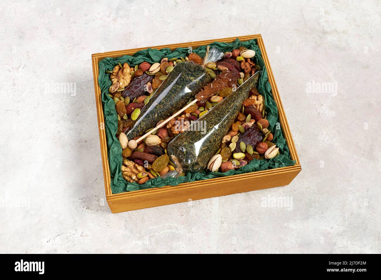 Una caja de madera llena de nueces, frutos secos y una bolsa de té verde como regalo Foto de stock