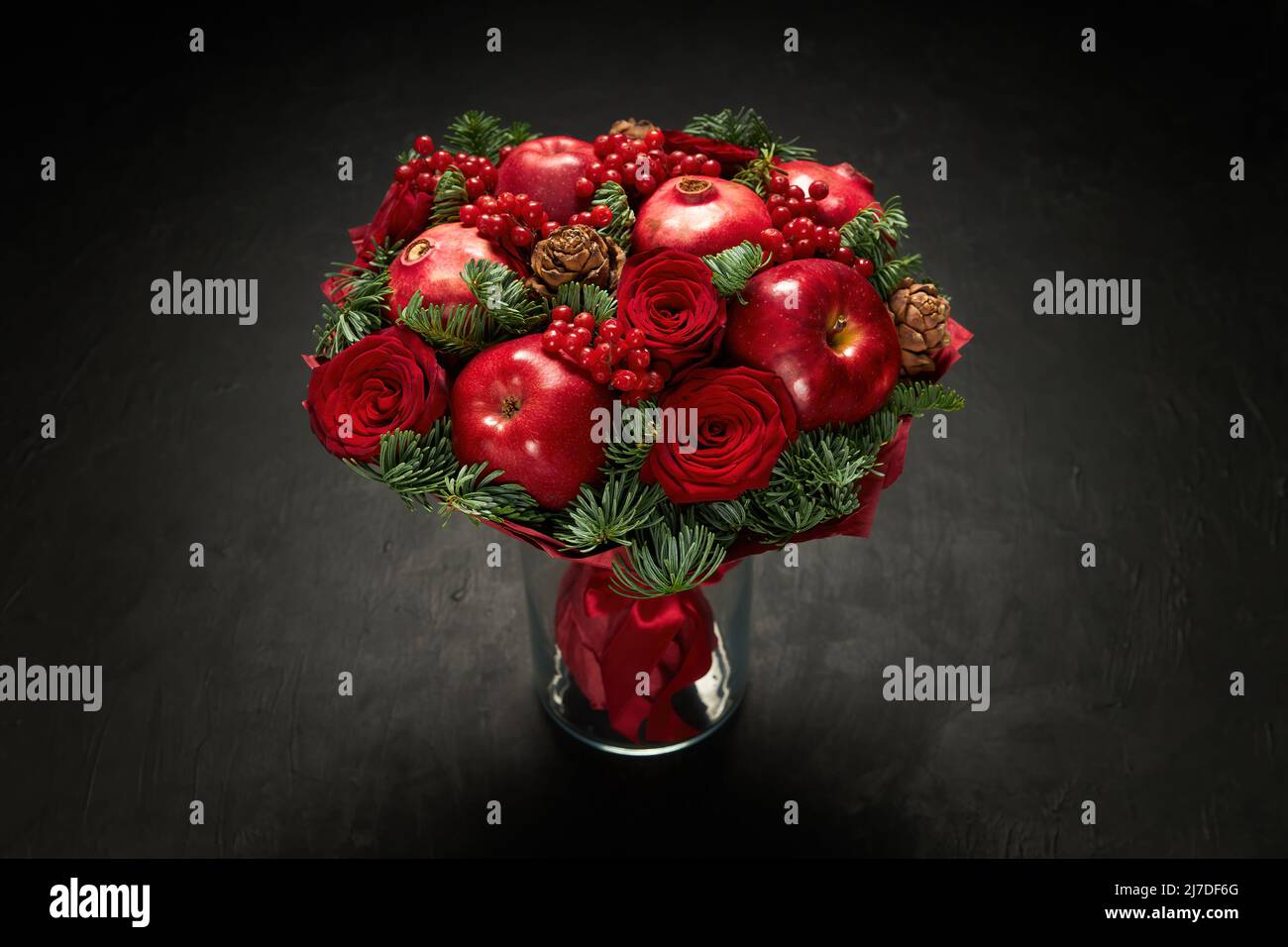 Hermoso bouquet de manzanas rojas, granadas y rosas rojas, decorado con ramitas de viburnum y abeto Foto de stock