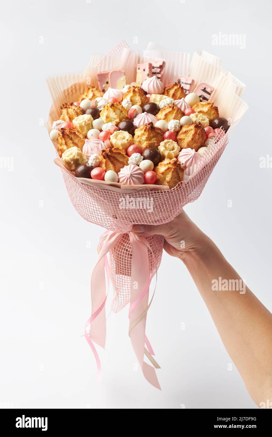 Divertido ramo de galletas, malvaviscos y chocolates en una mano femenina Foto de stock