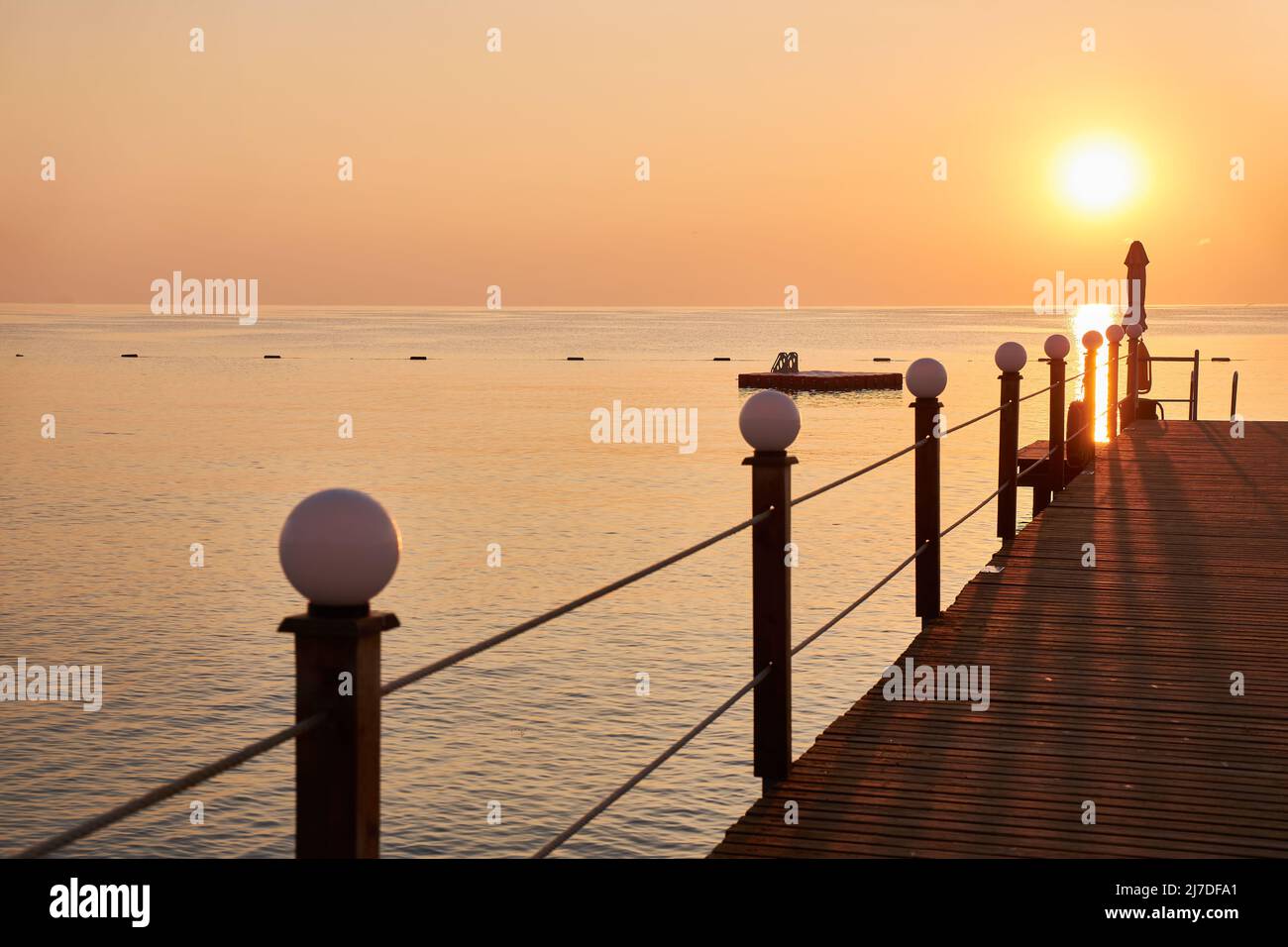 Muelle de madera en la playa sobre el fondo del cielo naranja y el sol naciente Foto de stock