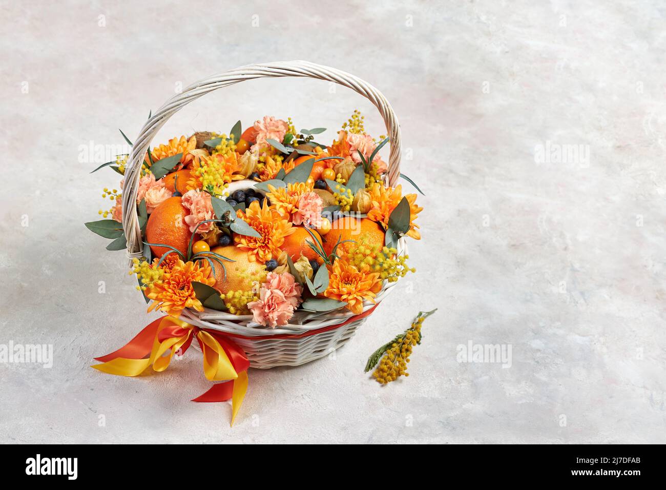 Cesta con frutas de color naranja y flores de color naranja sobre fondo gris Foto de stock