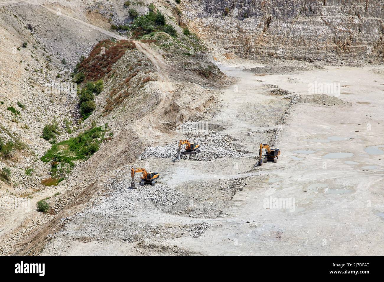 Tres excavadoras minan una piedra en el fondo de una gran cantera Foto de stock
