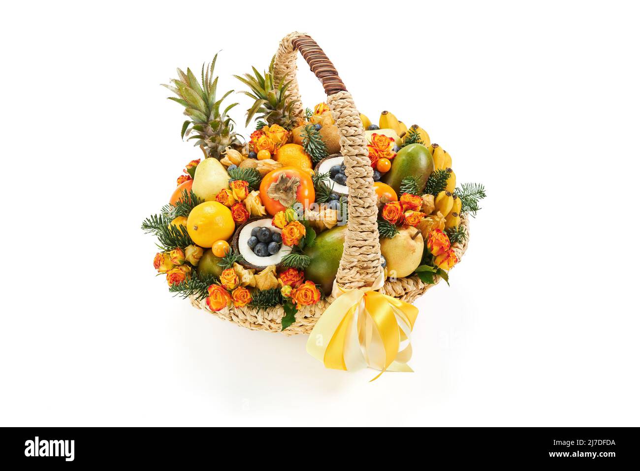 Gran cesta de mimbre llena de flores y frutas, decorada con ramitas de abeto sobre un fondo blanco Foto de stock