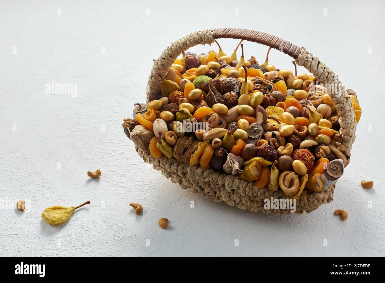 Cesta grande de mimbre llena de frutos secos y frutos secos sobre un fondo blanco Foto de stock