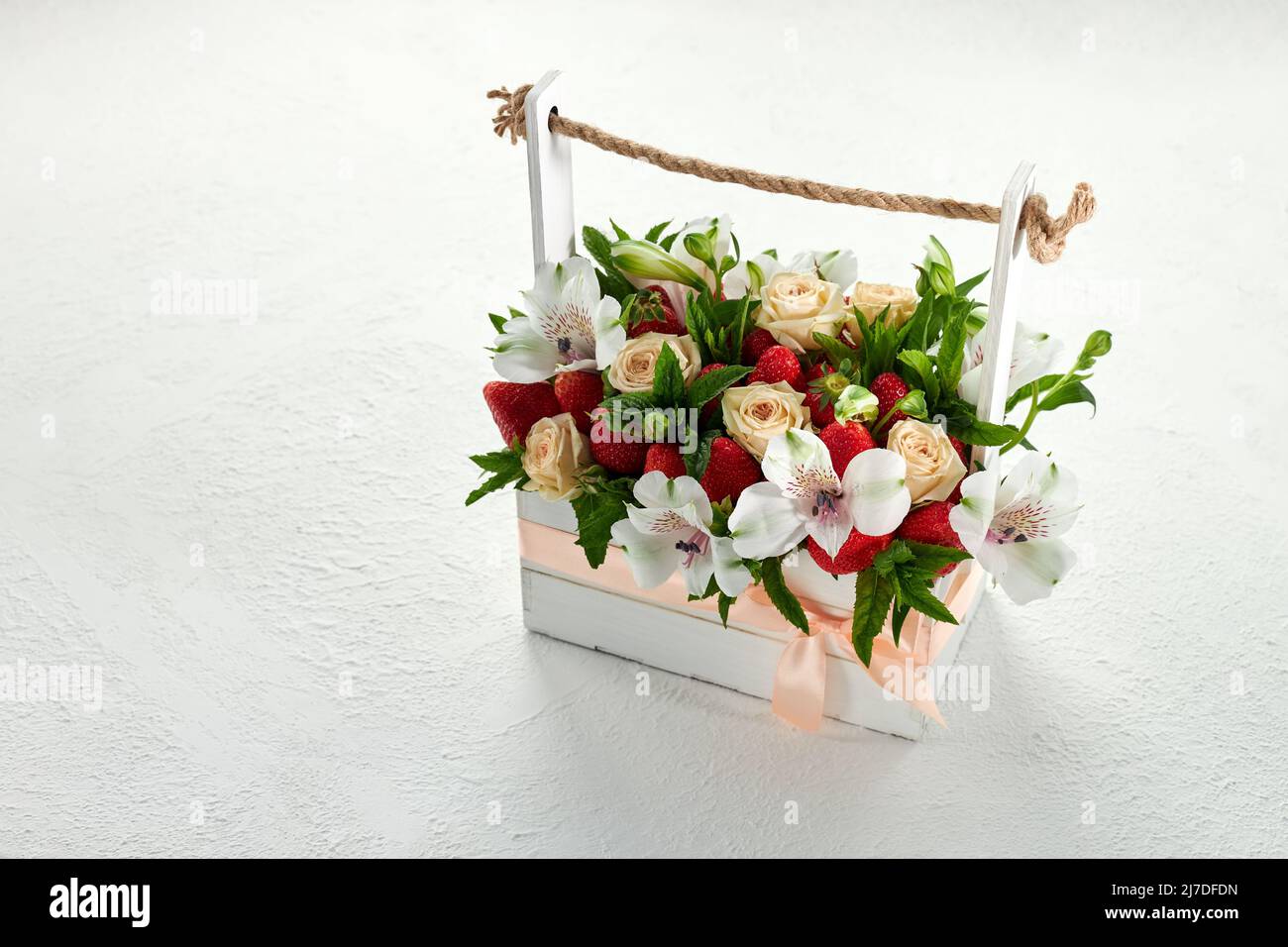 Caja de madera llena de fresas maduras y hermosas flores blancas y rosadas sobre un fondo blanco Foto de stock