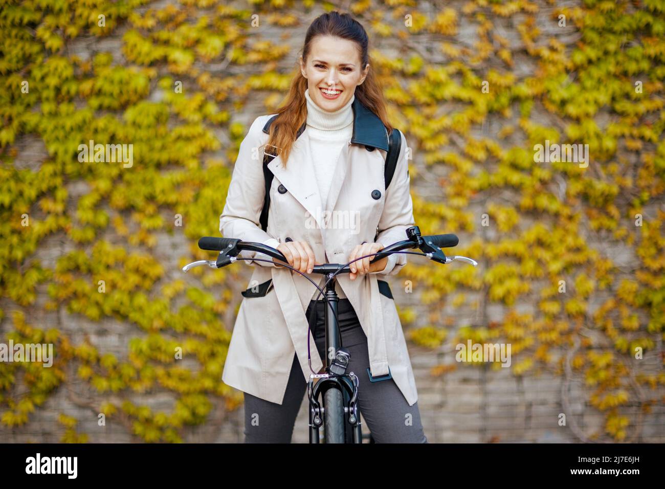 Corteza fondo Sinis Retrato de una mujer moderna sonriente en trenca beige con bicicleta contra  la pared verde exterior de la ciudad Fotografía de stock - Alamy