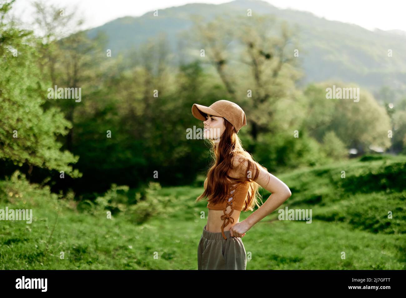 Una hermosa mujer en ropa deportiva y una gorra camina contra un paisaje  natural verde y sonríe a la luz del sol Fotografía de stock - Alamy