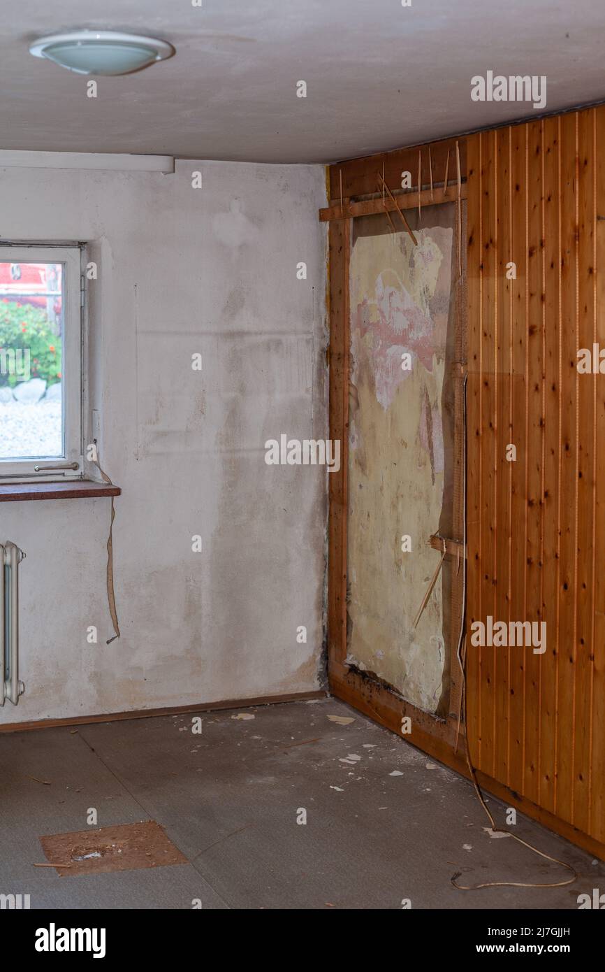 Detalle de una habitación con una vieja pared húmeda detrás de una pared de madera rota, pisos viejos, y un carrete de correa de shalusie roto Foto de stock